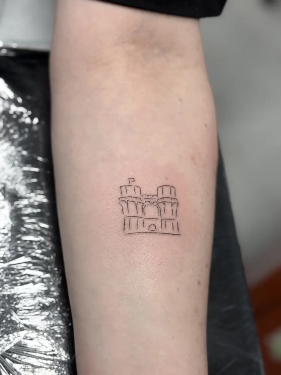 Mini tattoo de línea fina de unas torres de muralla en el antebrazo