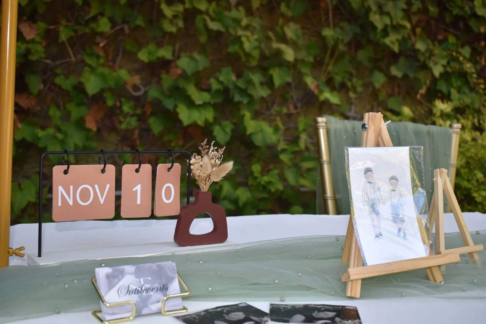 Detalle de la mesa: calendario de madera con NOV 10, jarrón con flores secas y un caballete con la ilustración de dos niños